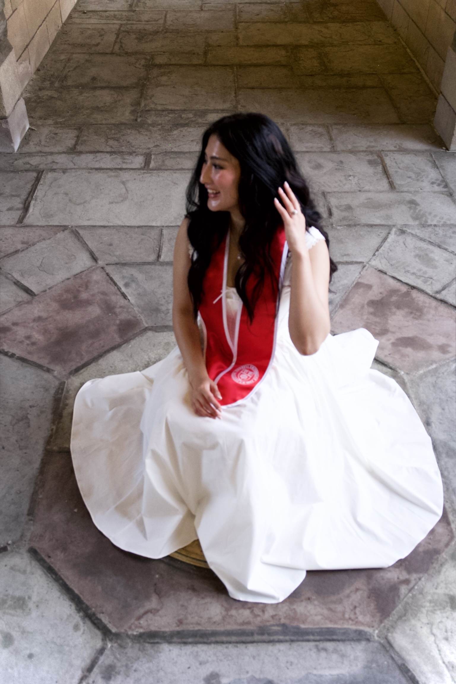Andisha Safdariyan seated in a white graduation dress on a stone floor